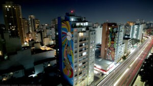 Foto extraída do time-lapse que documentou a execução do grafite "Metamorfose", de Marta Oliveira.. Mostra a emprena de um prédio com a pintura colorida.